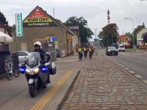 policjanci zabezpieczający przejazd rowerzystów. Policjant na motocyklu oraz rowerzyści.