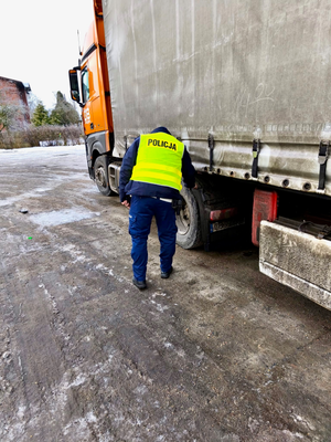 Obrazek przedstawiający policjanta stojącego przy samochodzie ciężarowym - kontrola drogowa