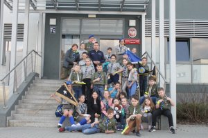 Grupa harcerzy i policjant stoją na schodach przed Komendą Powiatową Policji w Choszcznie w celu zrobienia pamiątkowego zdjęcia